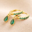 Green Crystal Huggie Hoop Earrings in Gold on Beige Fabric
