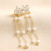 Crystal Flower and Pearl Chain Stud Earrings in Gold on Beige Fabric