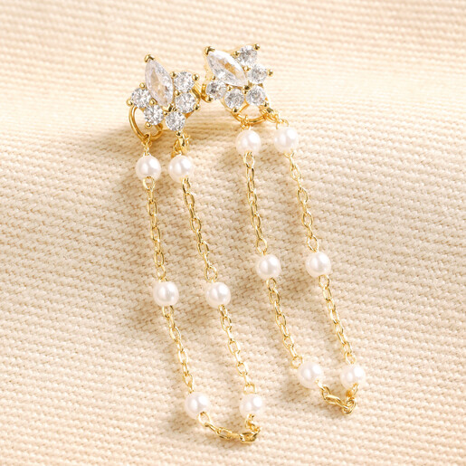 Crystal Flower and Pearl Chain Stud Earrings in Gold on Beige Fabric