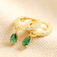 Green Teardrop Crystal Huggie Hoop Earrings in Gold on top of beige coloured fabric