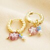 Millefiori Flower Bead Twisted Drop Huggie Hoop Earrings in Gold on top of beige coloured fabric