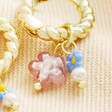 Close up of floral charms on Millefiori Flower Bead Twisted Drop Huggie Hoop Earrings in Gold against beige coloured fabric
