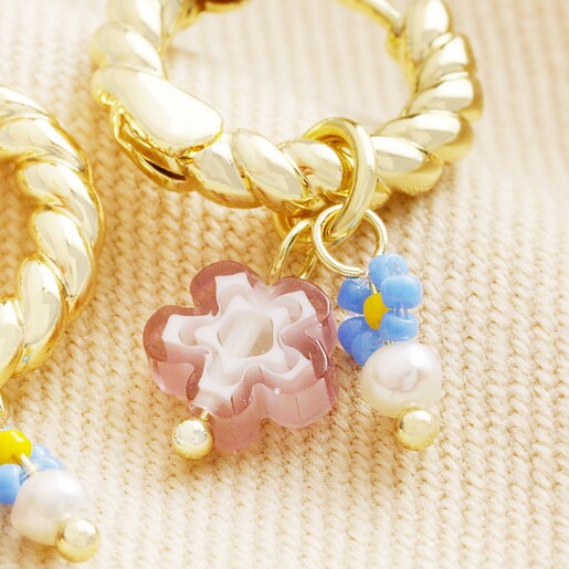 Close Up of Charms Close up of floral charms on Millefiori Flower Bead Twisted Drop Huggie Hoop Earrings in Gold against beige coloured fabric