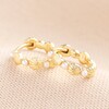 Pearl and Shell Huggie Hoop Earrings in Gold laid on top of beige coloured fabric