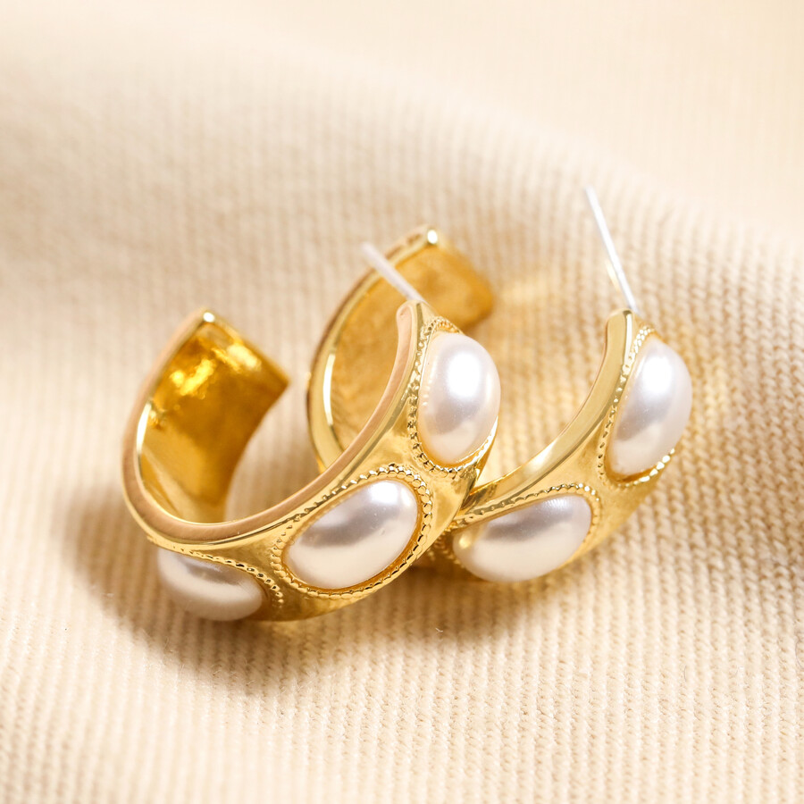 Chunky Oval Pearl Hoop Earrings in Gold laid on top of neutral coloured fabric