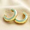 Teal Stone Hammered Hoop Earrings in Gold on beige Fabric