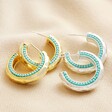 Teal Stone Hammered Hoop Earrings in Silver with Gold Version on Beige fabric