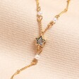 Close Up of Star on Shell Moon and Star Lariat Necklace in Gold on Beige Fabric
