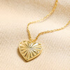 Close up of Sunbeam Heart Pendant Necklace in Gold against beige fabric
