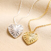 Close up of Sunbeam Heart Pendant Necklace in Silver with gold version on beige backdrop