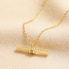 Close up of Crystal Feature T-Bar Pendant Necklace in Gold on top of beige coloured fabric