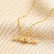 Close up of Crystal Feature T-Bar Pendant Necklace in Gold on top of beige coloured fabric