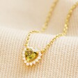 Tiny Green Crystal Heart Pendant Necklace in Gold on top of neutral coloured fabric