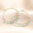 Big Metal London Medium Blue Beaded Hoop Earrings in Gold on Beige fabric