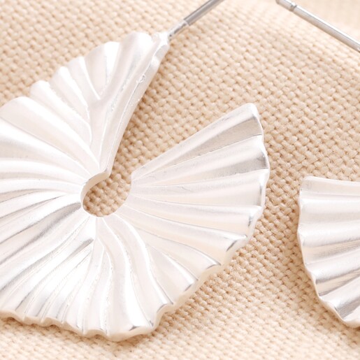 Close Up of Big Metal London Fan Leaf Hoop Earrings in Silver on Beige Fabric