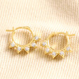 Estella Bartlett Crystal Sunburst Huggie Hoop Earrings in Gold on beige Fabric