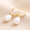 Pearl Drop Huggie Hoops in Gold on a Neutral Background