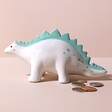 Dinosaur Money Box with coins outside against beige backdrop