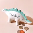 Personalised Dinosaur Money Box against beige backdrop with money outside