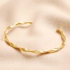Gold Stainless Steel Twisted Bangle on top of beige coloured material