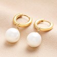 Gold Stainless Steel Large Pearl Drop Huggie Hoop Earrings Against Beige Background