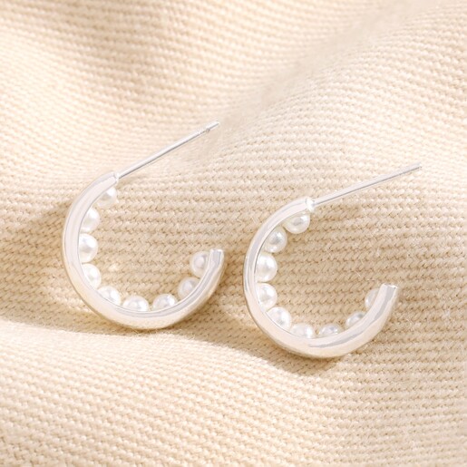 Encased Pearl Huggie Hoop Earrings in Silver on top of beige coloured fabric