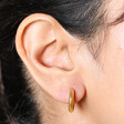 Close up of Gold Stainless Steel Huggie Hoop Earrings on model