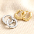 Stainless Steel Huggie Hoop Earrings with gold version on top of neutral coloured fabric