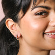 Model smiling wearing Stainless Steel Huggie Hoop Earrings in front of neutral backdrop