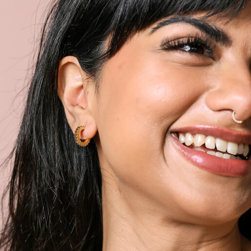 Gold Stainless Steel Ridged Huggie Hoop Earrings on model smiling against neutral background