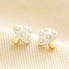 White Enamel Mushroom Stud Earrings in Gold on Beige Fabric