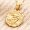 Close Up of Mermaid Coin Pendant Necklace in Gold on Beige Fabric