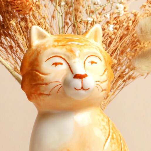 Close Up Close up of Tigger the Orange Cat Vase face with flowers behind