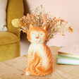 Close up of Tigger the Orange Cat Vase face sitting on table with flowers behind 