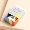 Tiny Matchbox Ceramic Rainbow Token open with token coming out of box against neutral backdrop