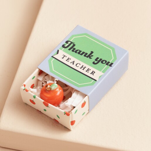 Tiny Matchbox Ceramic Apple Teacher Token open with apple in packaging against beige backdrop