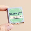 Model holding Tiny Matchbox Ceramic Apple Teacher Token against beige backdrop