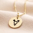 close up of the gold nonbinary charm on beige fabric