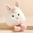 Jellycat Amuseabean Unicorn Soft Toy sat on top of raised beige surface
