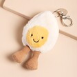 Jellycat Amuseable Happy Boiled Egg Bag Charm laying on pink surface