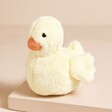Jellycat Fluffy Duck Soft Toy on top of beige surface