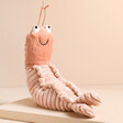 Jellycat Sheldon Shrimp Soft Toy on top of raised beige surface