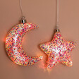 Personalised Hanging Pink Glitter LED Star Light with moon design lit up against beige backdrop
