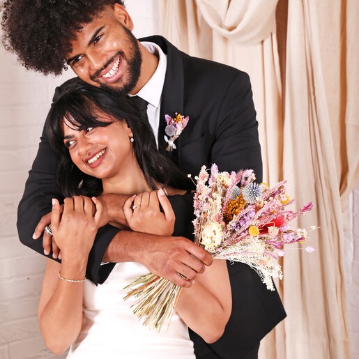A husband and wife embracing, he is wearing the buttonhole posy on his suit