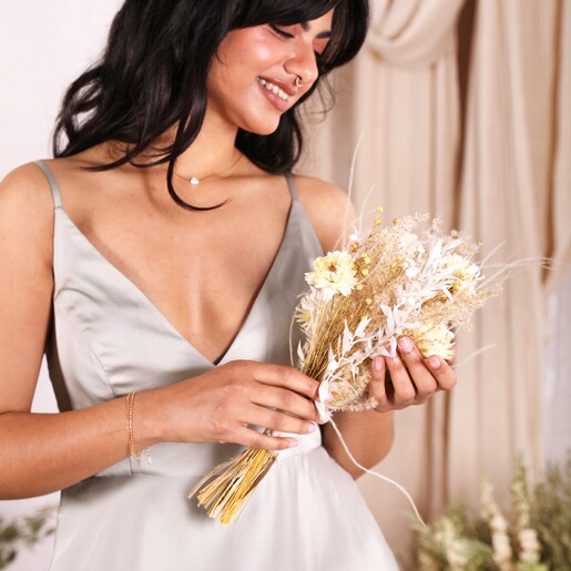 A bridesmaid in a green dress holding the posy and smiling at it