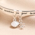 Close up of charms on Beach Lover Meaningful Word Bangle in Silver against beige material