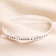 Laugh a Little Harder Meaningful Word Bangle in Silver on top of beige coloured fabric