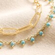 Close up of details on Teal Stone Droplet and Cable Chain Layered Bracelet in Gold against beige coloured material