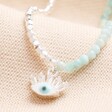 Close up of Blue Stone Beaded Evil Eye Pendant Necklace in Silver on Beige fabric
