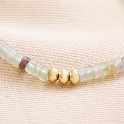 Close up of beads on Green Semi-Precious Stone Heishi Beaded Bracelet in Gold against beige fabric